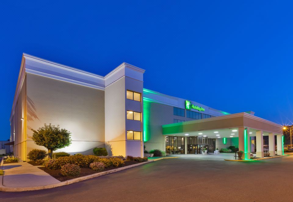 a large hotel building with a green and white sign , situated in a city at night at Holiday Inn Morgantown - Reading Area