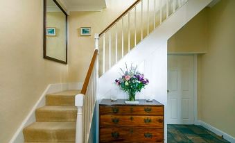 a staircase with a wooden railing , a vase of flowers on the landing , and a mirror above the door at Home Farm Boreham