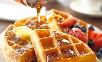 a plate of waffles topped with butter , syrup , and fruit , placed on a dining table at Country Inn & Suites by Radisson, Emporia, VA