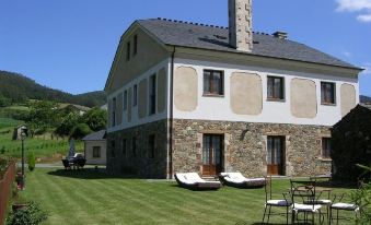 a large house with a stone wall and two beds on the lawn , surrounded by green grass and trees at El Castro