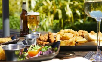 a dining table with a plate of food , including fried fish and onion rings , accompanied by a glass of beer at The Mayfield Seamer