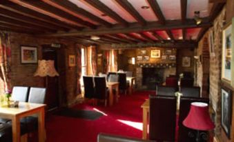 a dining room with red carpet , wooden beams on the ceiling , and several chairs and tables arranged around them at The Royal Oak