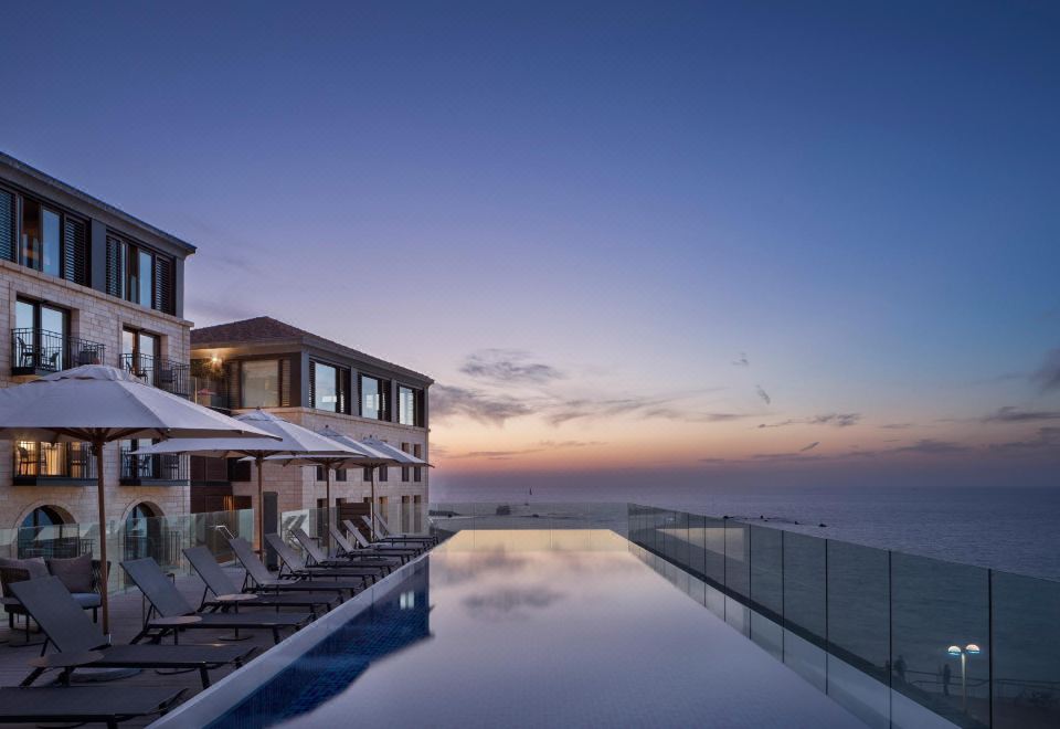 a large swimming pool with a view of the ocean and a house in the background at The Setai Tel Aviv, a Member of the Leading Hotels of the World