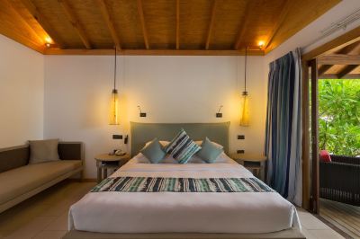 a large bed with white linens and a green headboard is in a room with wooden floors and two lamps on the wall at Vilamendhoo Island Resort & Spa