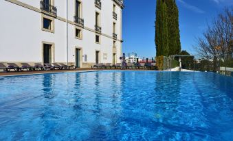 a large swimming pool with blue water and sun loungers in front of a white building at Pousada De Viseu