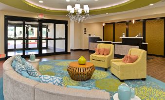 a modern hotel lobby with yellow and green furniture , a round table , and a chandelier at Homewood Suites by Hilton Houma