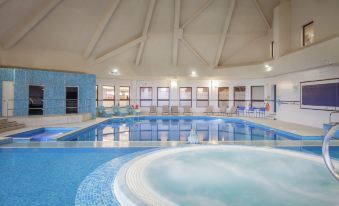 an indoor swimming pool with a hot tub , surrounded by lounge chairs and windows , providing a relaxing atmosphere at DoubleTree by Hilton Glasgow Westerwood Spa & Golf Resort