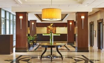 a well - lit hotel lobby with a round table in the center , surrounded by chairs and couches at Sheraton Suites Chicago Elk Grove