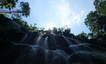 The sun shines through a waterfall, surrounded by trees on both sides at Joaquim's Lodge