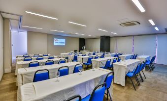 a conference room with blue chairs and white tables , a screen on the wall , and a projector screen at the front at San Marino Suites Hotel by Nobile