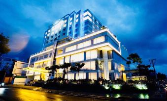 a large hotel building surrounded by palm trees , located in a city at night at Saigon Vinh Long Hotel