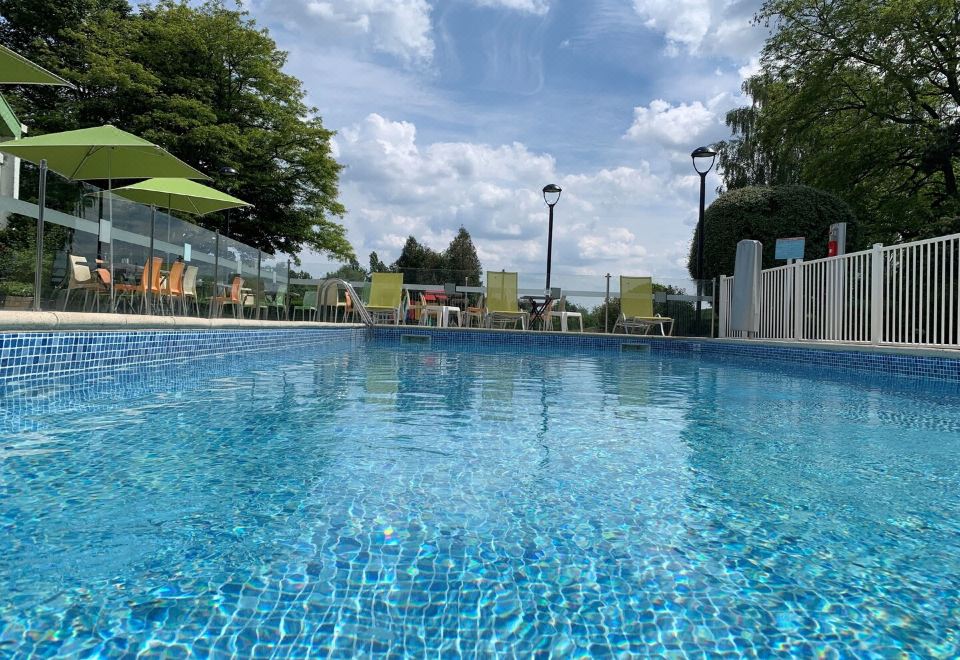 a large blue swimming pool surrounded by green grass , with several lounge chairs and umbrellas placed around it at Holiday Inn Lille - Ouest Englos