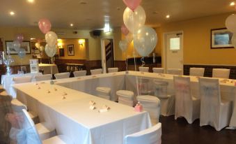 a long banquet table with white tablecloths and pink balloons is set up in a room at The Pheasant Inn