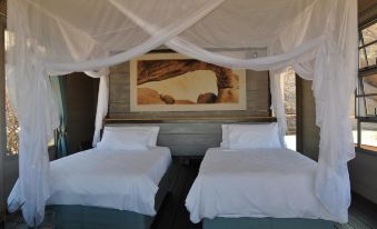a room with two beds , one on the left and one on the right , both covered with white sheets at Spitzkoppen Lodge