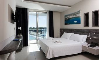 a modern bedroom with a large window offering a view of the ocean , white bedding on the bed , and black curtains at Hotel Belvedere