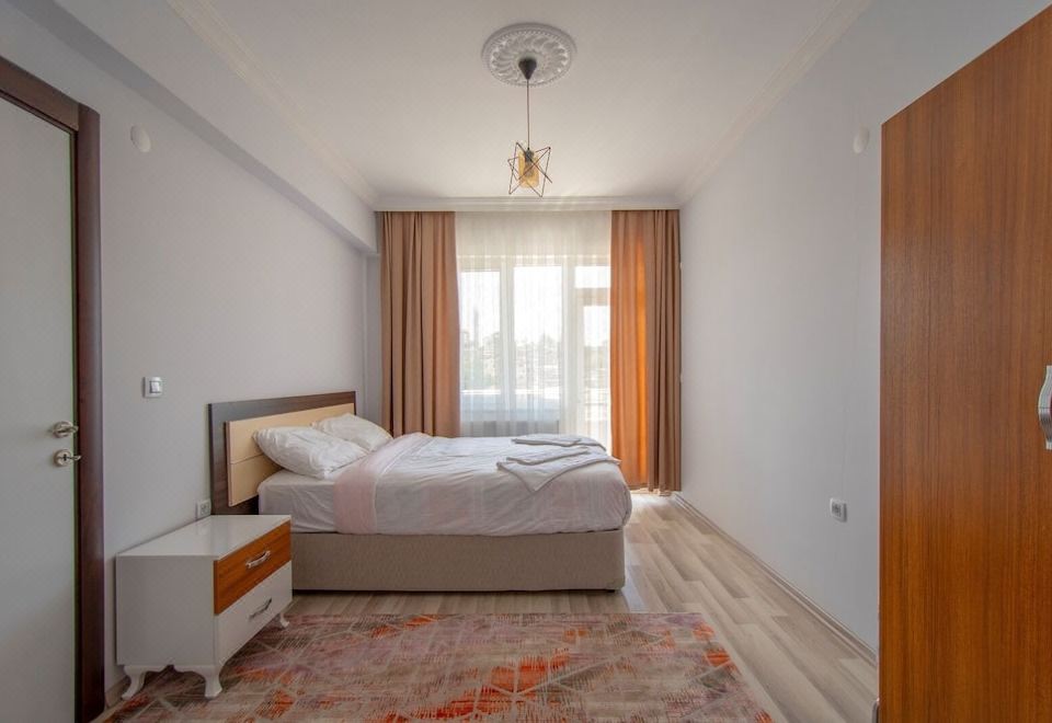 a modern bedroom with white walls , wooden floors , and a large window , featuring a bed with white bedding and an orange curtain at Prime Inn