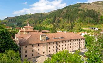 a large , brown building with a red roof and a tower is surrounded by trees and other buildings at Parador Monasterio de Corias