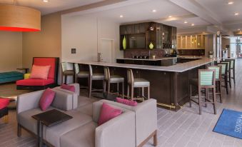 a modern living room with a bar area , featuring pink and gray furniture and white carpeting at Hilton Garden Inn Bristol