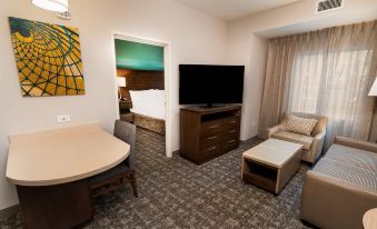 a modern living room with a couch , dining table , and television in front of a bedroom at Staybridge Suites Washington DC East - Largo