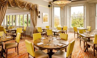 a large dining room with yellow chairs and tables , a chandelier hanging from the ceiling at Mercure Bristol North the Grange Hotel