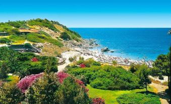 a scenic view of a coastal area with lush greenery and a body of water in the background at Falkensteiner Resort Capo Boi