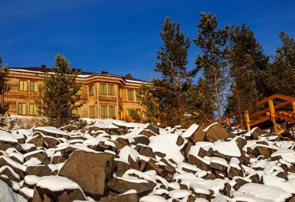 a large wooden building with a red roof is surrounded by rocks and trees , with snow on the ground at Luxe
