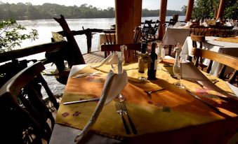 a table is set with a yellow tablecloth , silverware , wine glasses , and napkins overlooking a body of water at Laguna Lodge