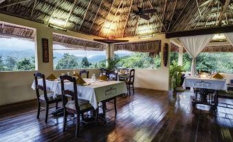 a room with a wooden floor and tables set up for dining , overlooking a mountain view at Sleeping Giant Rainforest Lodge