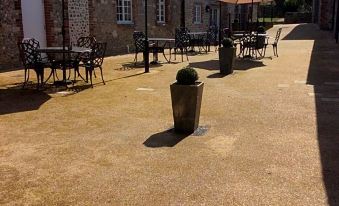 a paved courtyard surrounded by buildings , with several umbrellas placed around the area for outdoor dining at The New Inn