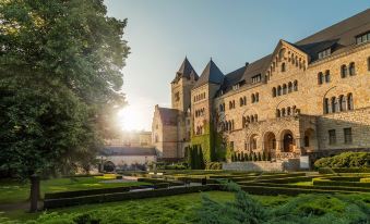a grand stone castle surrounded by lush green gardens , with the sun setting behind the castle at Sheraton Poznan Hotel