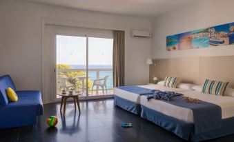 a hotel room with two beds , a table , and a window overlooking the ocean , all decorated in blue and white at Htop Caleta Palace #HtopBliss