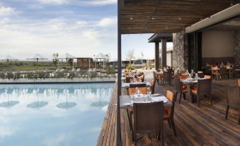 a large swimming pool is surrounded by a patio with tables and chairs , creating an inviting outdoor dining area at The Vines Resort & Spa
