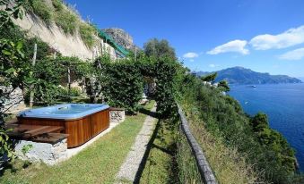 a large wooden hot tub is surrounded by greenery and overlooks the ocean from a balcony at Villa Maria