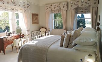 a luxurious bedroom with white beddings , a large window , and a chandelier , as well as a bed with beige linens and pillows at Cleatham Hall