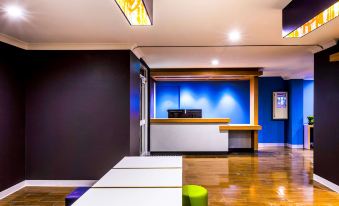 a modern office lobby with blue walls , wooden floors , and white tables , as well as a reception desk at ibis budget Casula Liverpool