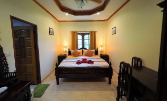 a well - lit bedroom with a wooden bed , white bedding , and red towels , along with a dining table and chairs at Stella Resort
