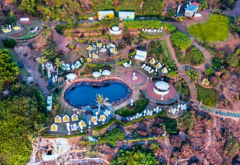 aerial view of a resort with multiple pools , gardens , and buildings surrounded by greenery , including a building on the right side at W Goa