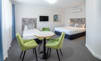 a hotel room with two beds , a dining table , and green chairs , along with a tv on the wall at Bridge Motel