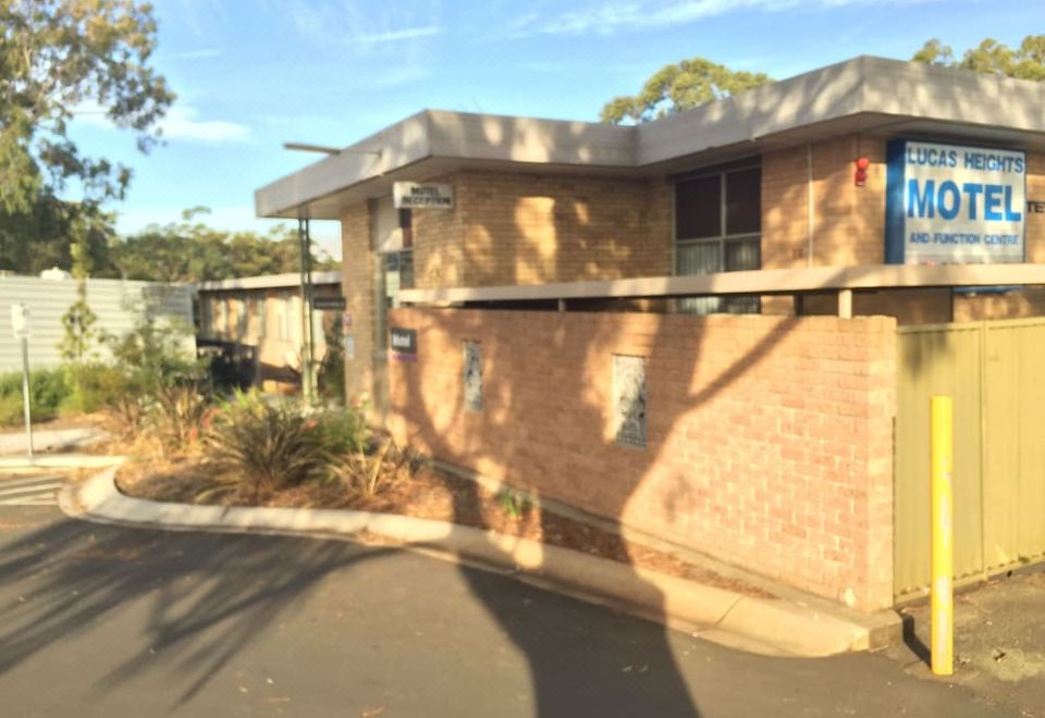 a brick house with a brown roof and a blue door is situated next to a tree at Lucas Heights Motel