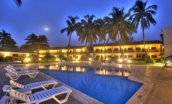 a resort with a pool surrounded by palm trees , lights reflecting off the water , and lounge chairs at Sunset Beach Hotel