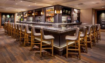 a modern bar with wooden stools and marble countertops , featuring a variety of drinks on display at Marriott Boston Quincy