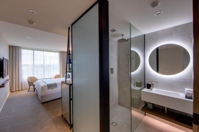 a modern bedroom with a large bed , a bathroom with a shower and sink , and a walk - in closet at Oval Hotel at Adelaide Oval, an EVT hotel