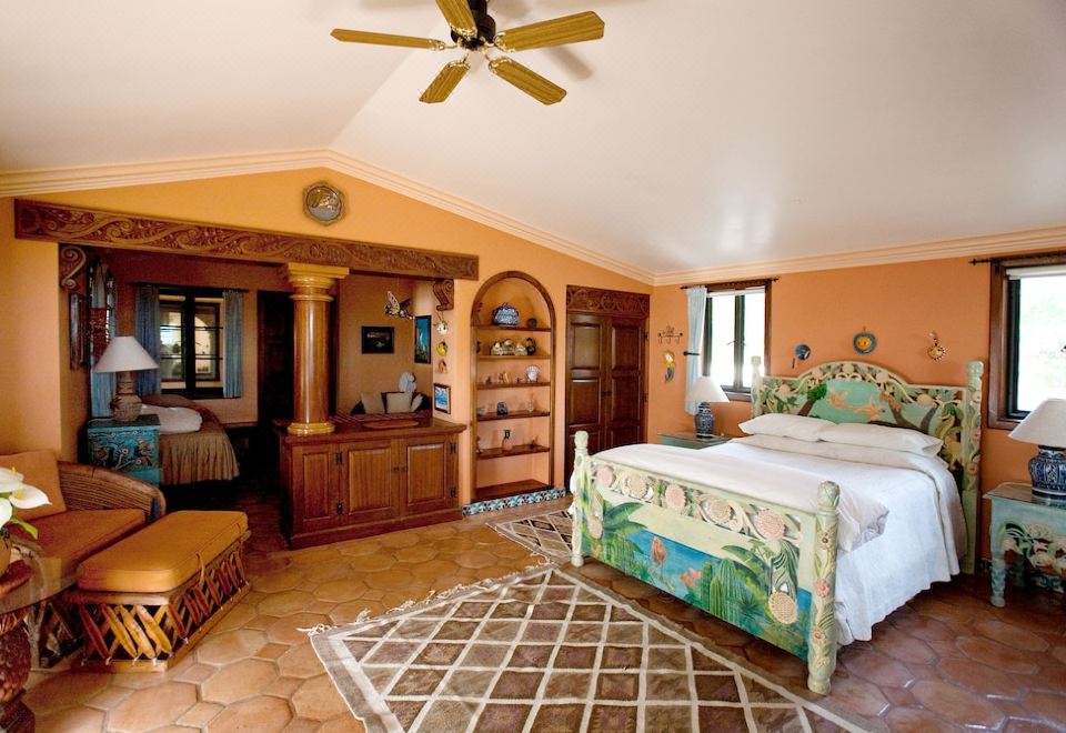 a bedroom with a large bed , wooden dresser , and ceiling fan , decorated with tropical plants at Villa del Faro