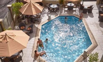 a rooftop pool surrounded by umbrellas and tables , with people enjoying their time in the pool at Tradewinds Hotel