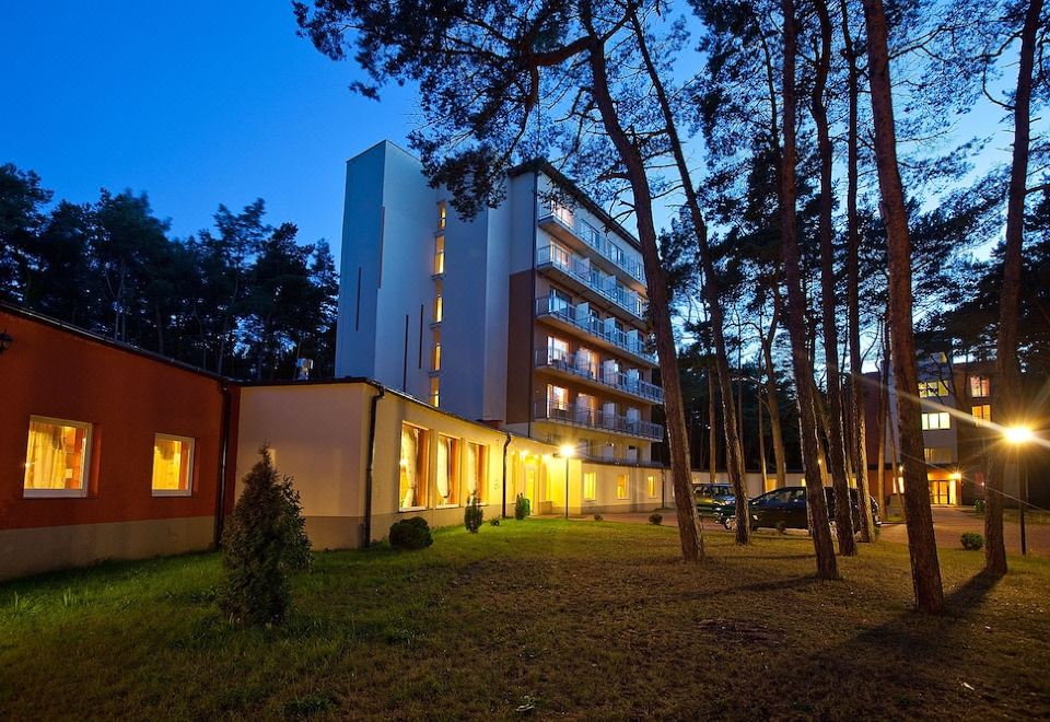 a large white building with a green roof is surrounded by trees at night , with the sun casting a warm glow at Millennium Spa