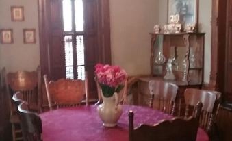 a dining room with a wooden dining table surrounded by chairs , and a vase of flowers placed on the table at Smithville Historical Museum and Inn