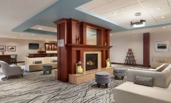 a large , modern living room with a fireplace , comfortable seating , and a bar area under a high ceiling at Hilton Garden Inn Troy