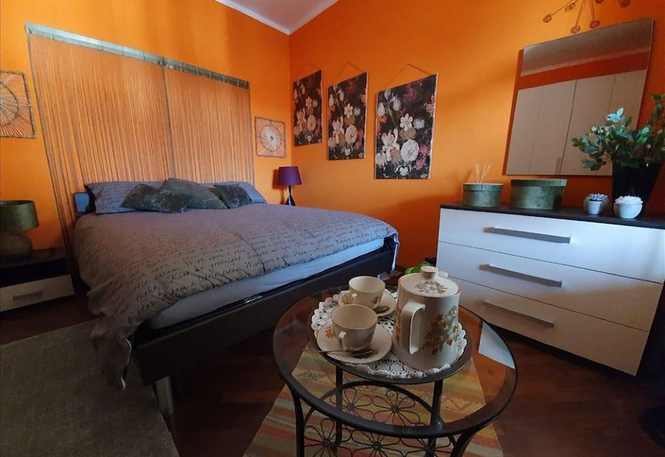 a bedroom with an orange wall , a bed , and a glass table holding a cup and teapot at CasAda