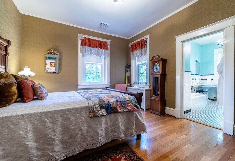 a cozy bedroom with hardwood floors , a large bed , and a door leading to another room at Hillcrest Mansion Inn