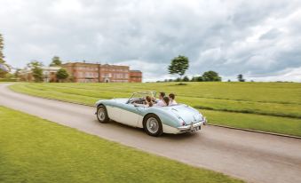 a blue and white vintage car with a couple of people driving on the road , driving past a large building at Four Seasons Hotel Hampshire
